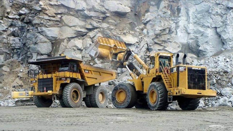 Loader and haul truck working beside a rock face